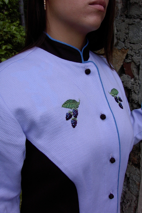 Close up image of small blackberry embroidery on the chest of Women's Chef Coat style BSW104; Shown in Lavender & black, 100% cotton petti point pique & 100% cotton Gabardine, two front hip tailored welt pockets, Copen piping (collar, front, cuffs & pockets), Black Gabardine, hand tied knot buttons & blackberry embroideries on the chests, pockets, & back of collar.